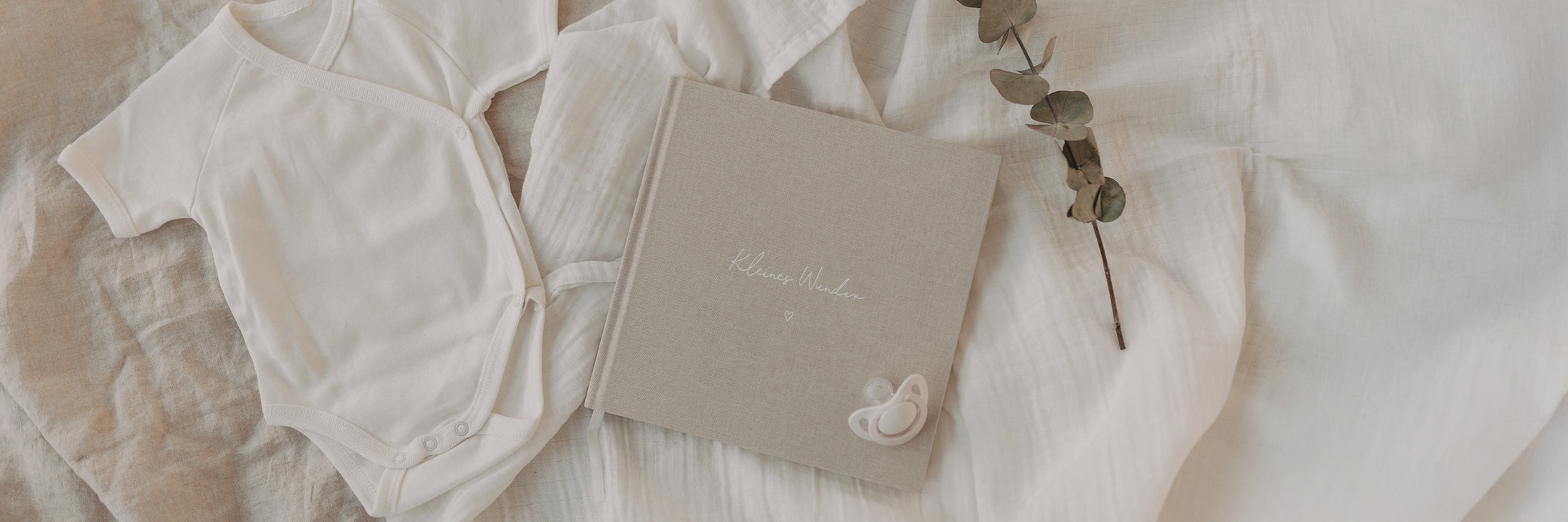 Beiges Leinen-Babybuch mit der Aufschrift „Kleines Wunder“ in weißer Schrift liegt auf einer weichen Decke. Im Bild steht: „Unser neues Schwangerschaftsbuch begleitet dich durch diese besondere Zeit“ und unten „Schwangerschaftsbuch“