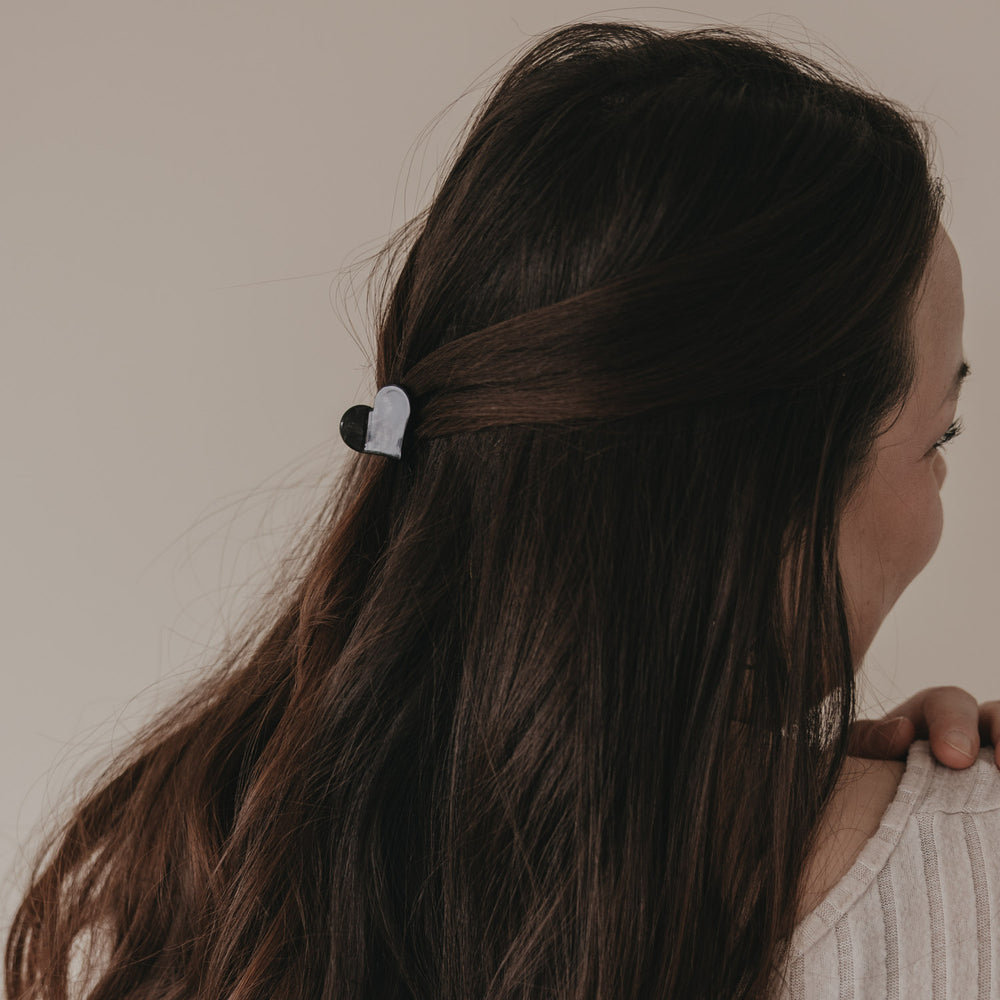 Kleine Haarspange in Herzform schwarz hält halboffenes braunes Haar seitlich zusammen