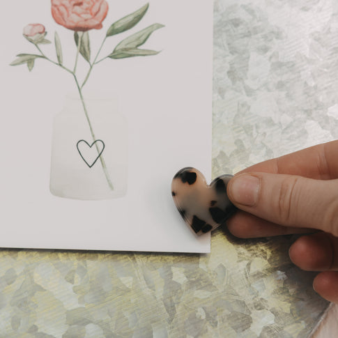 Herzförmiger Magnet im Leo-Look hält eine Blumenkarte an einer magnetischen Pinnwand