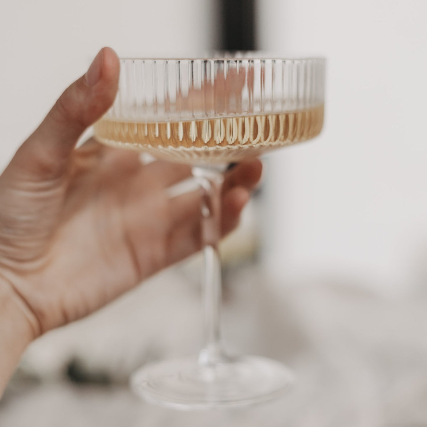 Hand mit gefülltem Champagnerglas in Nahaufnahme – schlichte Eleganz und feine Riffelstruktur.