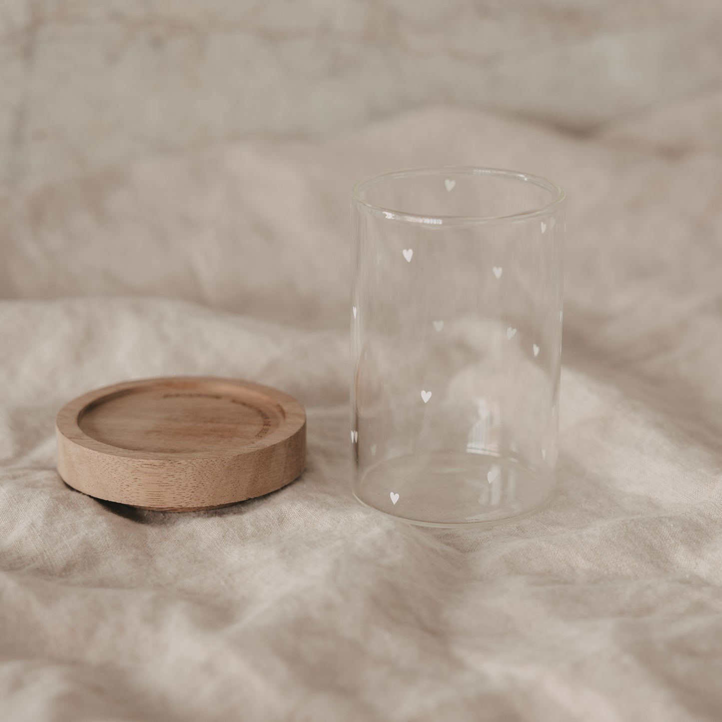 Minivorratsglas mit weißen Herzen und abgenommenem Holzdeckel auf Stoff
