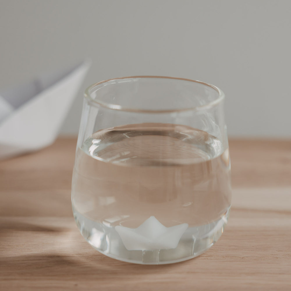 Trinkglas mit Papierboot Motiv gefüllt mit Wasser, schlichtes Glas auf Holzoberfläche