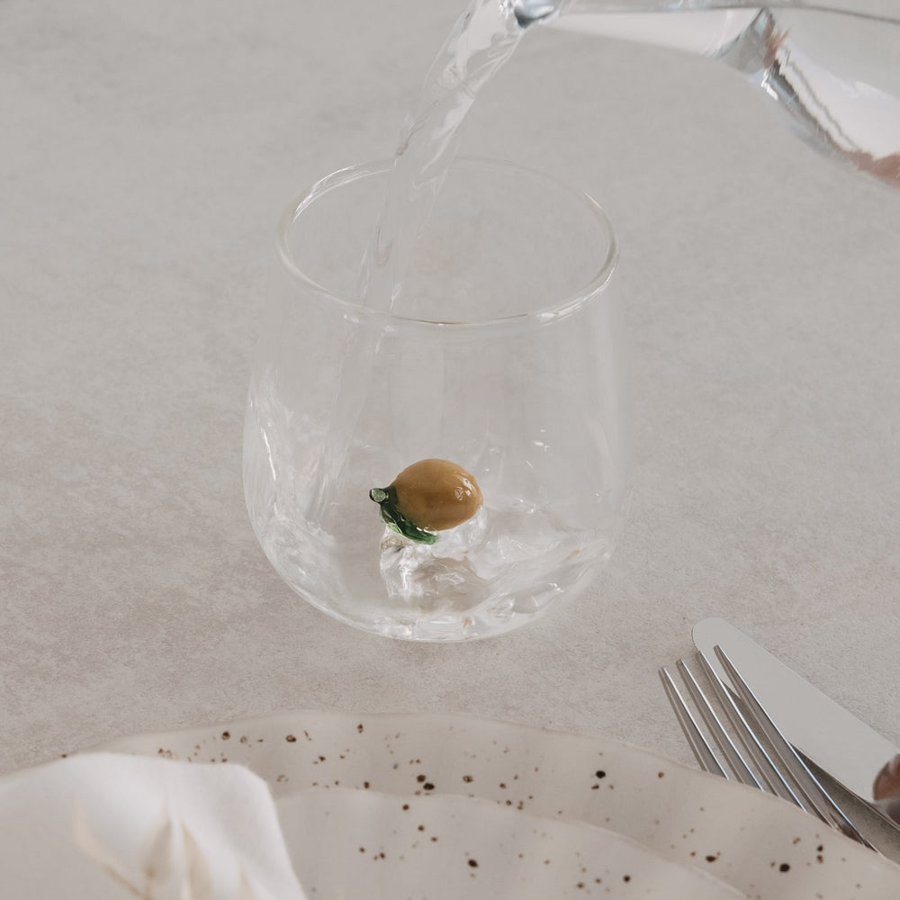 Zitronenfigur wird mit Wasser befüllt, modernes Designglas für Getränke auf gedecktem Tisch

