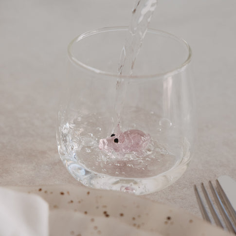 Trinkglas mit rosa Schwein im Boden, Wasser wird eingegossen, modernes Glasdesign