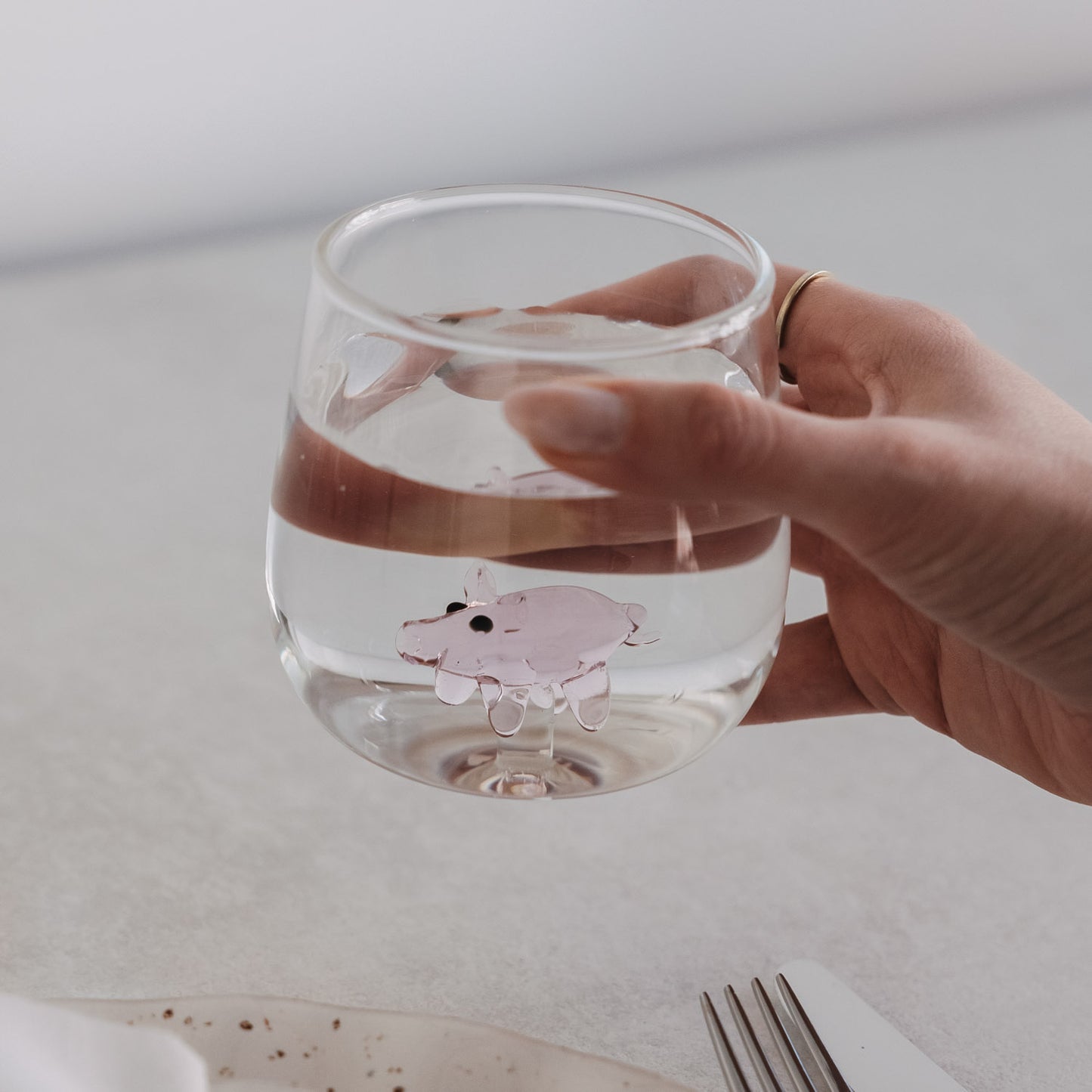 Glas mit Schwein-Motiv, gefüllt mit Wasser, auf gedecktem Tisch mit Besteck