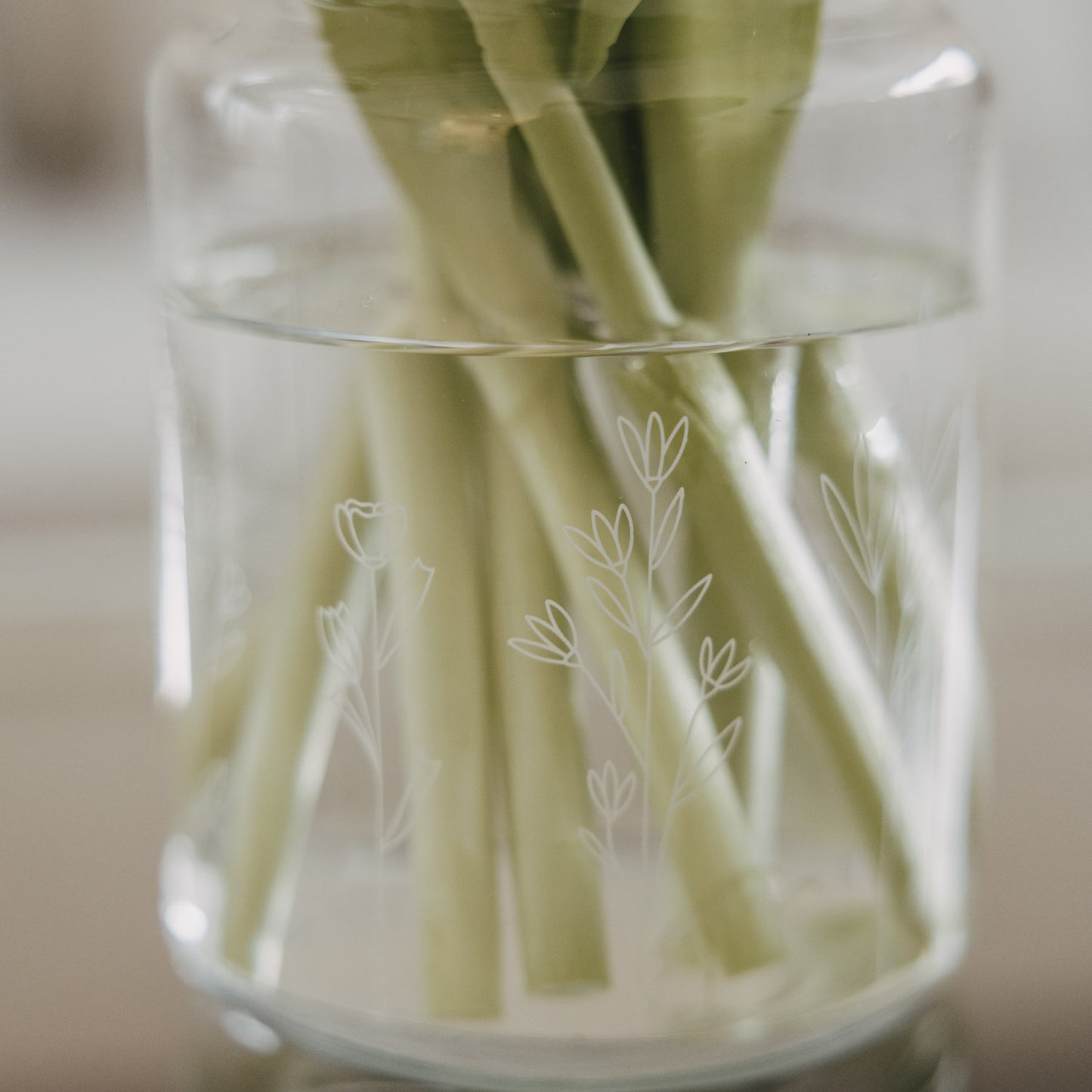 Detail Glasvase mit Blumenmotiv und Tulpenstielen im Wasser, natürliche Optik