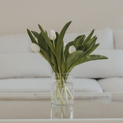 Glasvase mit Blumenwiesen-Motiv und weißen Tulpen, dekorativ auf Glastisch