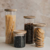 Vier Vorratsgläser mit weißen Herzen und Holzdeckeln, gefüllt mit Spaghetti, Linsen, Müsli und Keksen