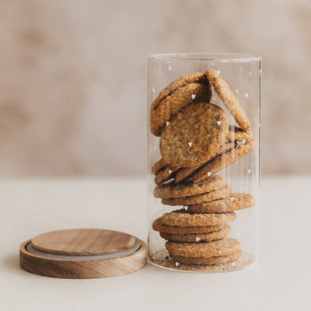 Offenes Vorratsglas mit weißen Herzen und Keksen, daneben der abgenommene Holzdeckel