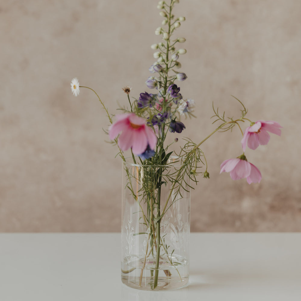 Hoher Glasbehälter mit weißem Wildblumen-Motiv und Holzdeckel, als Vase mit bunten Wiesenblumen dekoriert