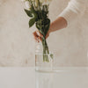Hand stellt weißen Blumenstrauß in Glasvase mit Herzmotiv