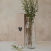 Glas Karaffe mit Blumenmotiv und frischen Zweigen, neben Verpackung mit Herzmotiv