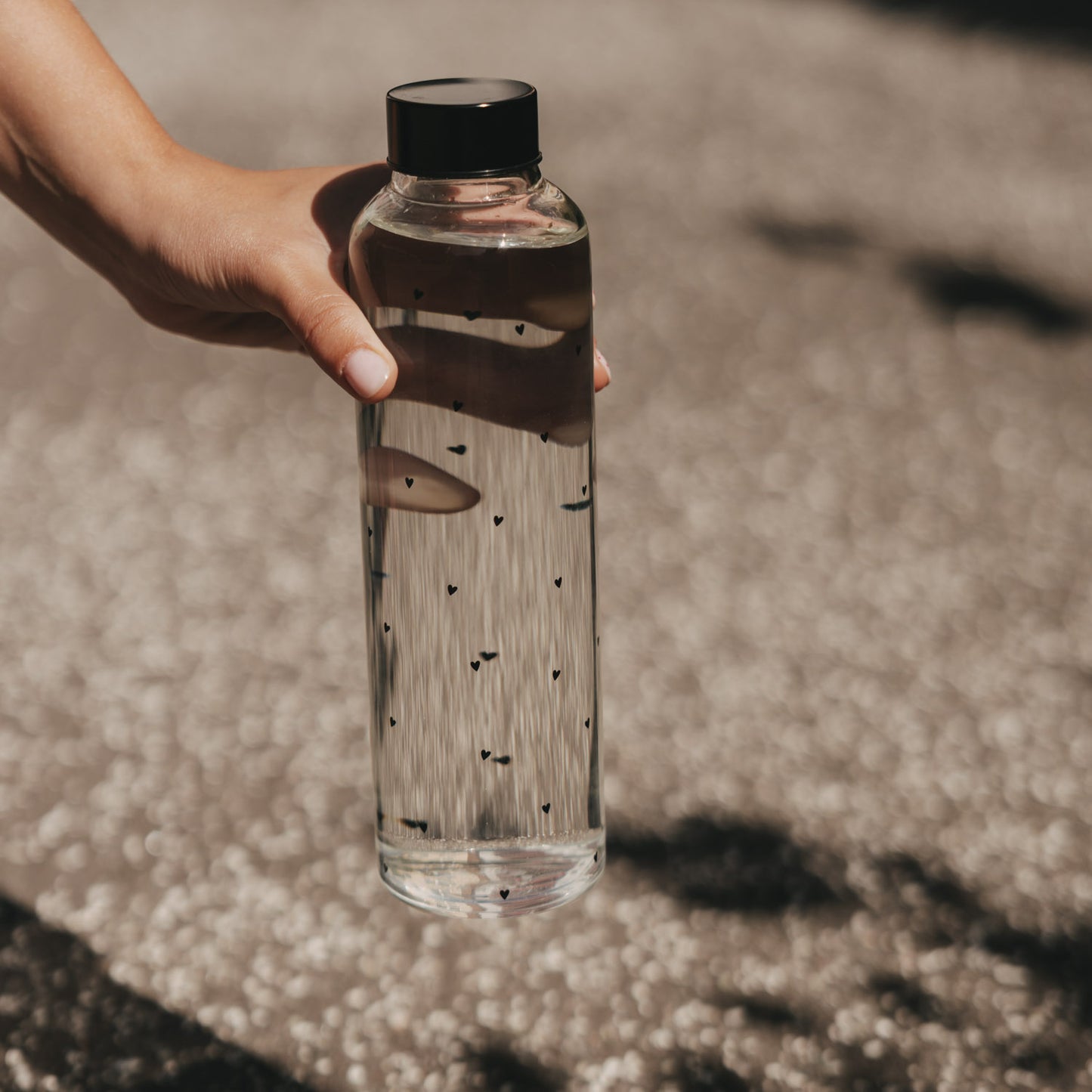 Glas Trinkflasche mit kleinen Herzen 750 ml, in der Hand gehalten, Sonnenlicht und Schatten im Freien