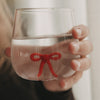 Nahaufnahme eines transparenten Trinkglases mit roter Schleifenfigur im Glasboden, gefüllt mit Wasser.