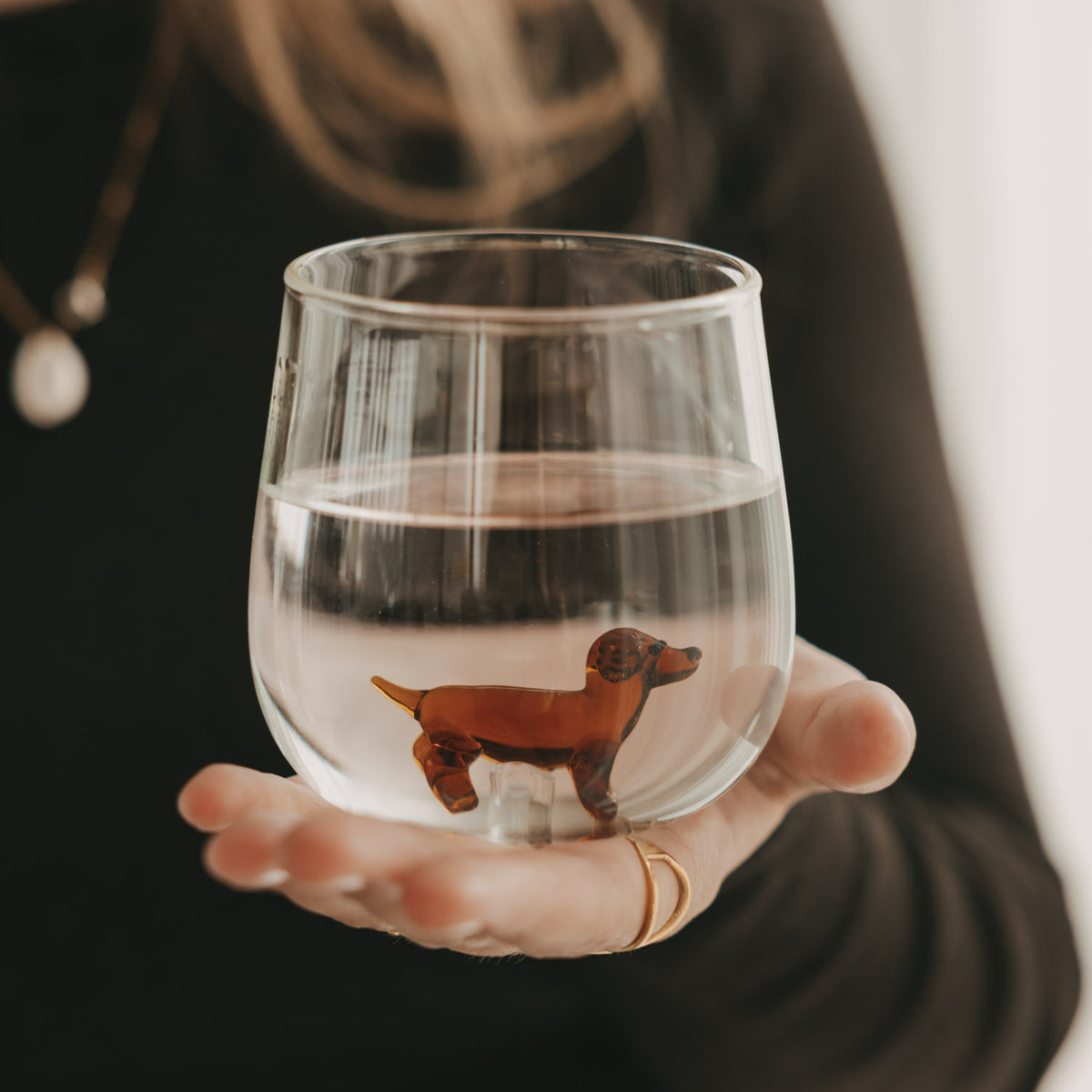 Transparentes Figurenglas mit braunem Dackel im Glasboden, mit Wasser gefüllt und auf einer Hand präsentiert.