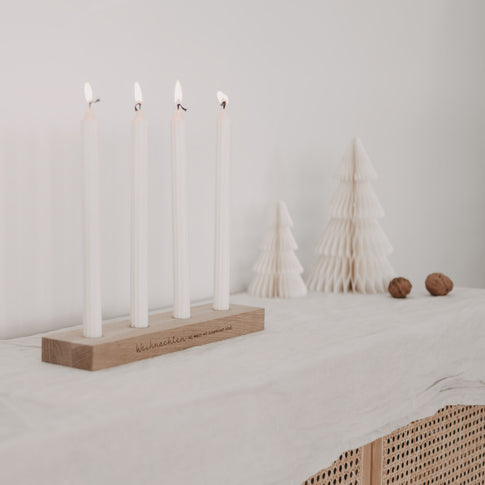 Weihnachtlicher Kerzenhalter mit vier Kerzen auf Tisch, im Hintergrund Papier-Tannenbäume