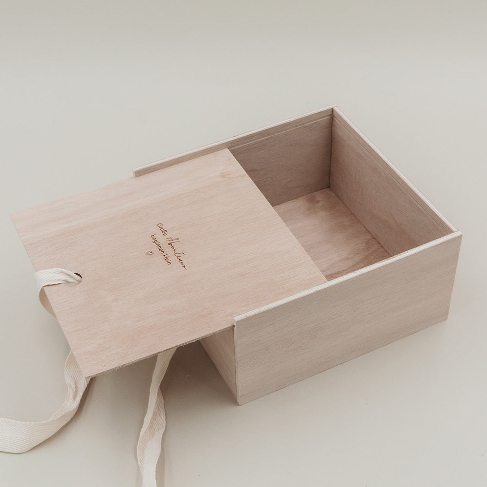 Offene Erinnerungsbox aus Holz mit herausgezogener Schiebeklappe und cremefarbener Schleife.