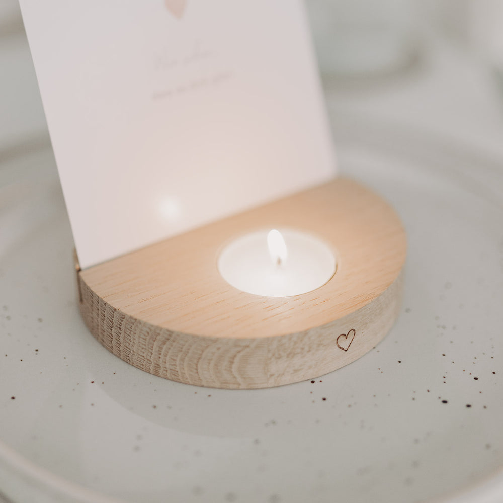 Nahaufnahme des Holz-Teelichthalters mit Herzgravur und brennendem Teelicht im Vordergrund.