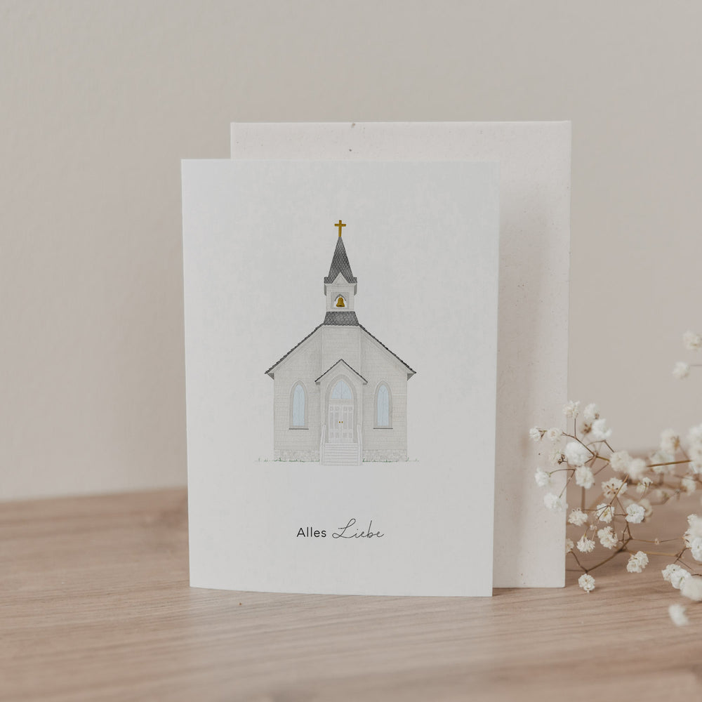 Klappkarte mit handgezeichneter Kirche und Schrift „Alles Liebe“, stehend mit Umschlag auf Holzoberfläche neben Trockenblumen.