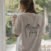 Frau mit Brille und LOVE-T-Shirt steht mit Kaffeetasse am Fenster