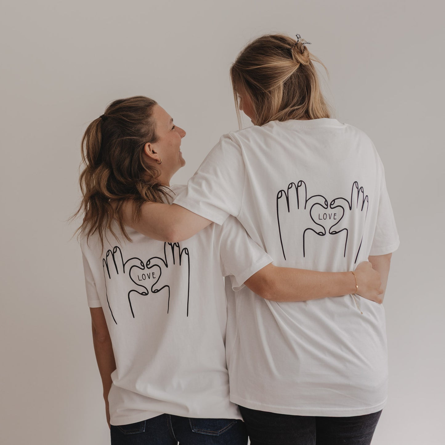 Zwei Frauen mit LOVE-T-Shirts umarmen sich lachend von hinten