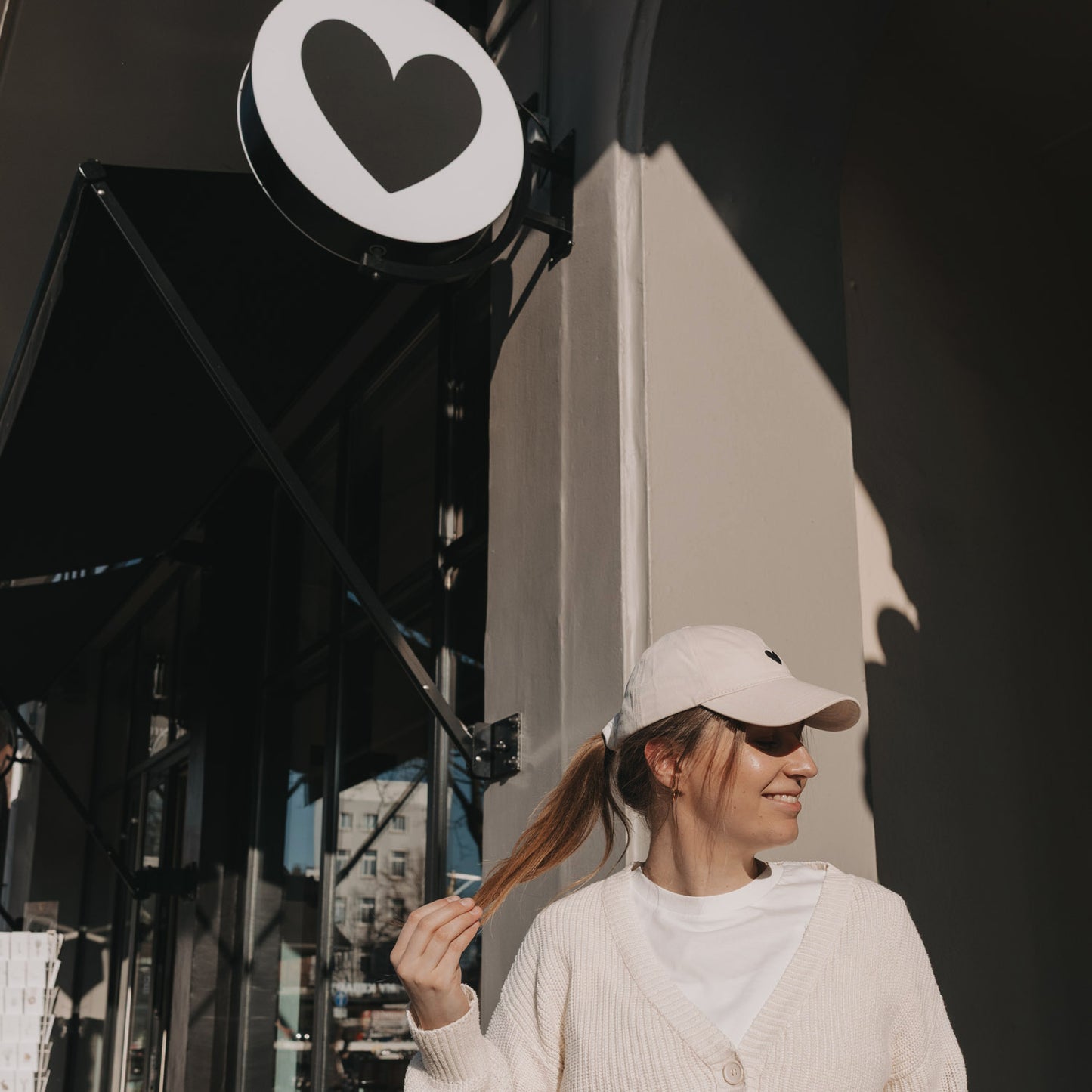 Frau mit beiger Herz-Cap vor Eulenschnitt Geschäft, Lifestyle Aufnahme im Sonnenlicht