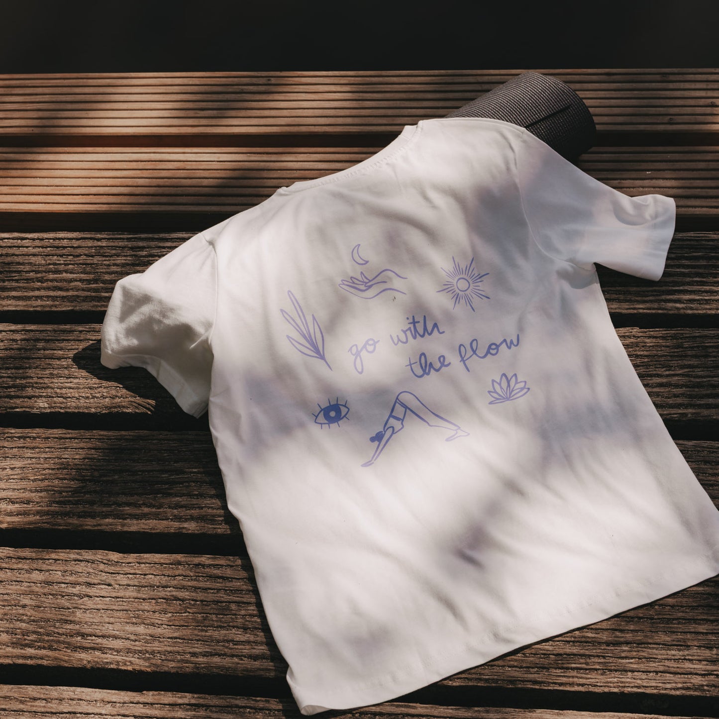Weißes T-Shirt mit „go with the flow“ Aufdruck, flach auf Holzsteg im Sonnenlicht