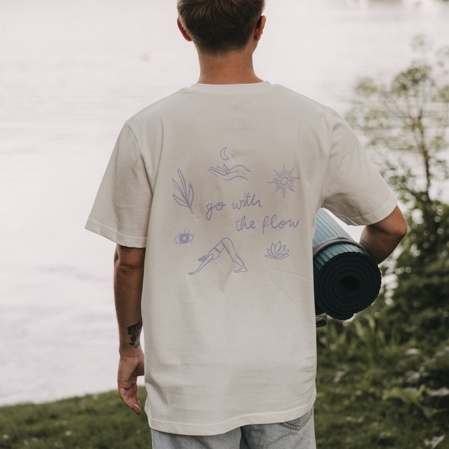 Person von hinten mit Yogamatte, weißes T-Shirt „go with the flow“ mit großem Rückendruck