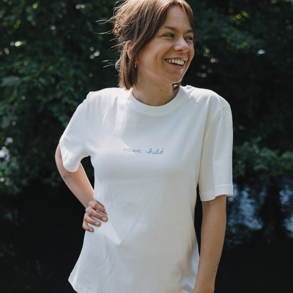 Frau im weißen „Ocean Child“ T-Shirt mit Frontprint, natürlicher Outdoor Look