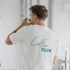 Mann im weißen „Coffee Club“ T-Shirt, Rückenansicht beim Kaffeetrinken