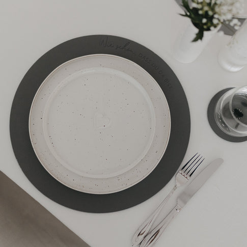 Wendbares Platzset in Grau mit Prägung „Wie schön, dass du da bist“ auf gedecktem Tisch.
