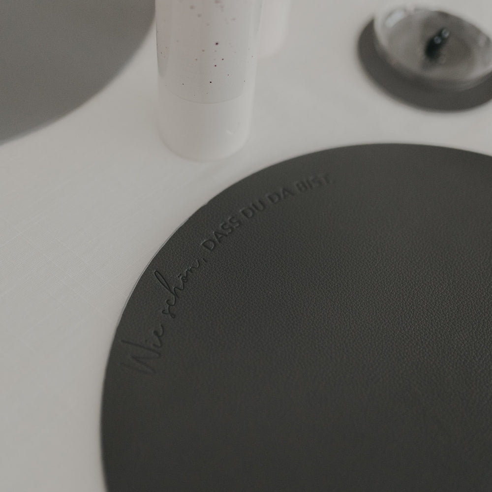 Detailaufnahme des grauen Platzsets mit geprägtem Schriftzug „Wie schön, dass du da bist“.