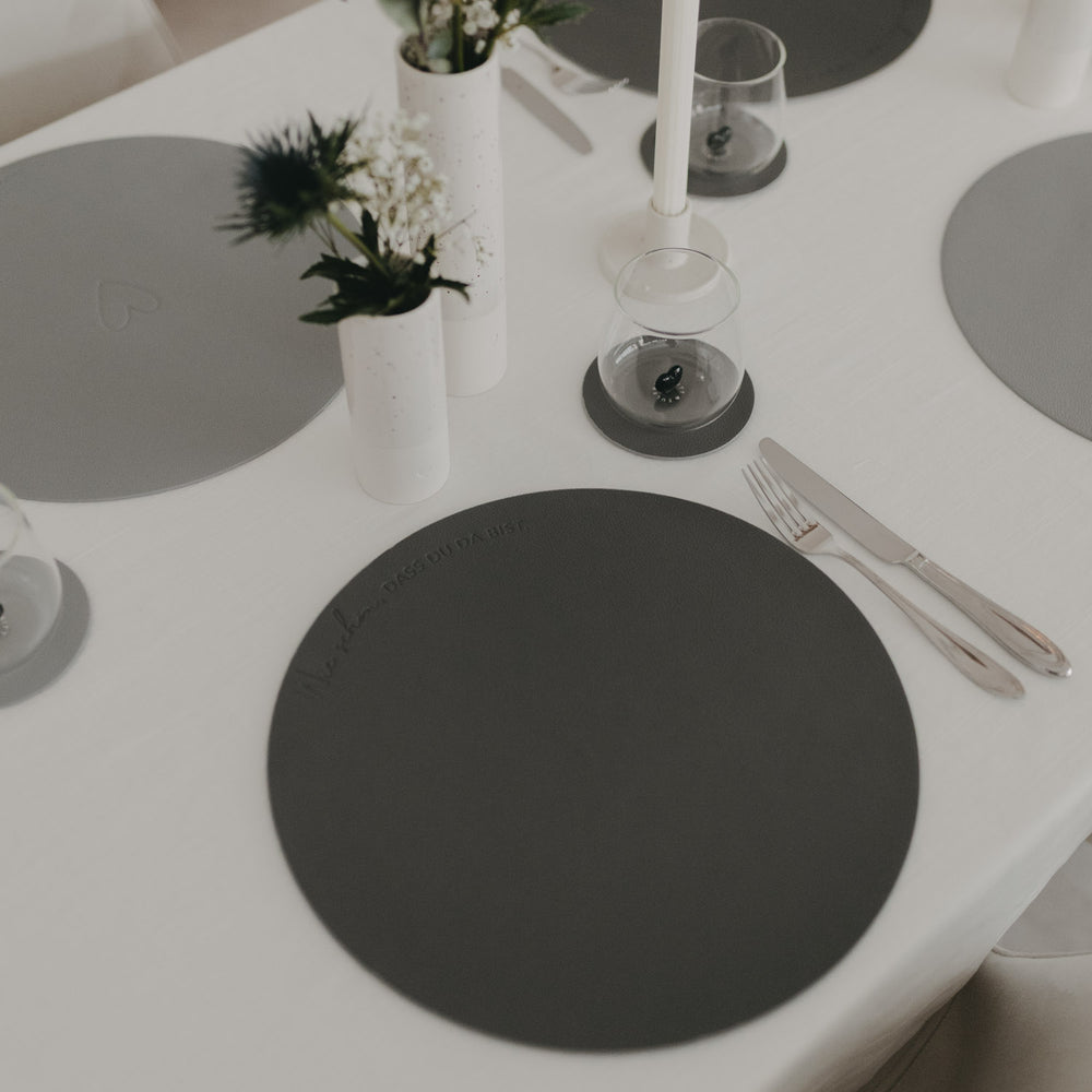 Gedeckter Tisch mit grauem, rundem Platzset und modernem, minimalistischem Tischarrangement.