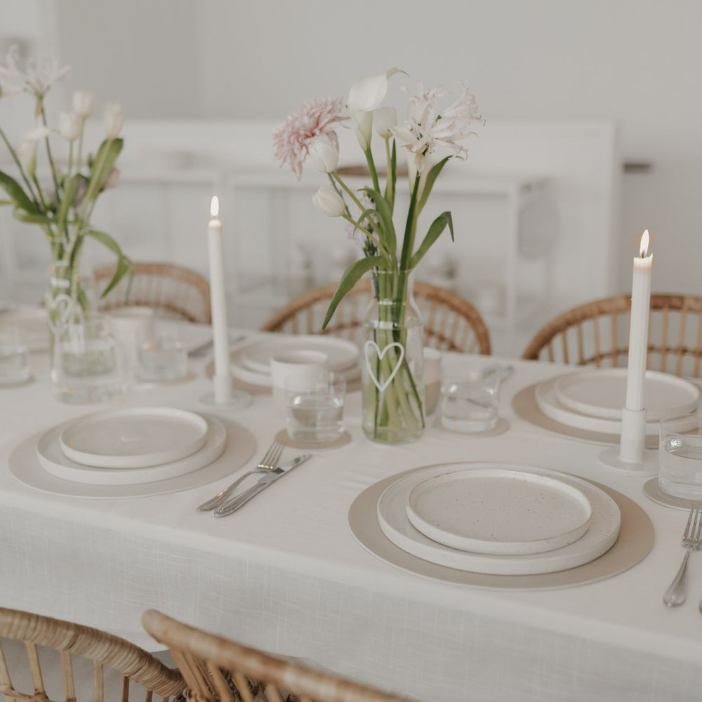 Festlich gedeckter Tisch mit hellen runden Platzsets und Herzmotiv in Creme.