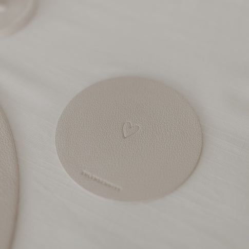 Cremefarbener Untersetzer mit geprägtem Herz neben Tischset und Besteck auf heller Tischdecke.