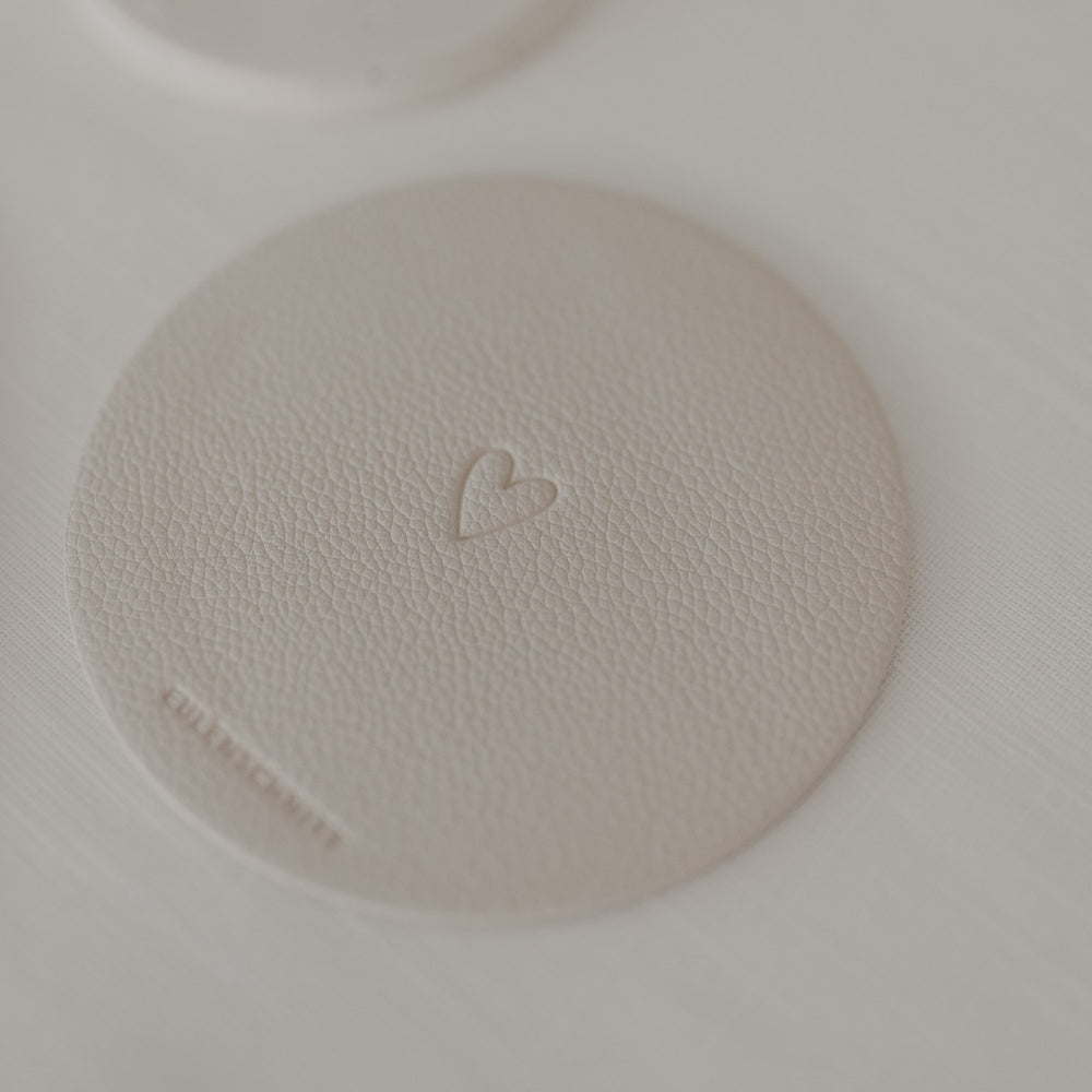 Beiger runder Untersetzer mit Herzprägung auf weißer Tischdecke.