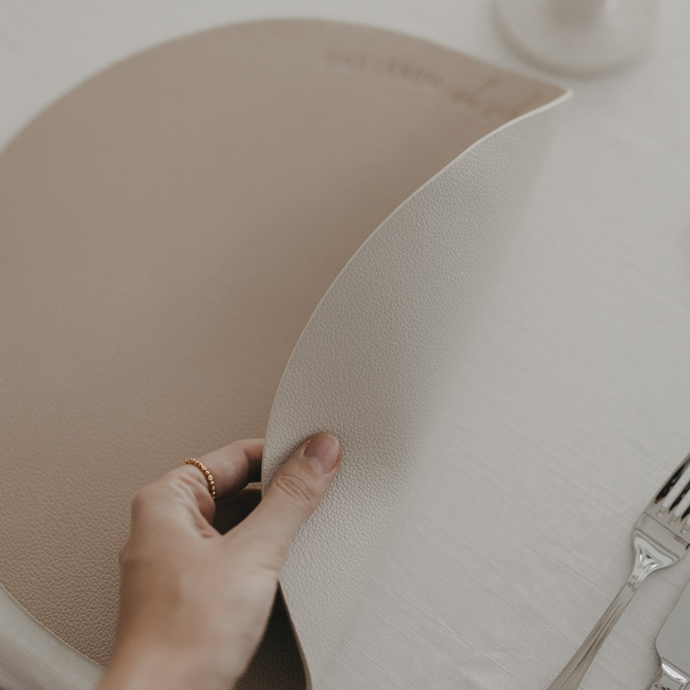 Wendbares Platzset in Creme wird angehoben, zeigt flexible Kunstlederstruktur für stilvolle Tischdeko.