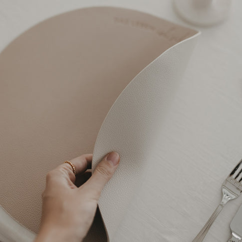 Wendbares Platzset in Creme wird angehoben, zeigt flexible Kunstlederstruktur für stilvolle Tischdeko.