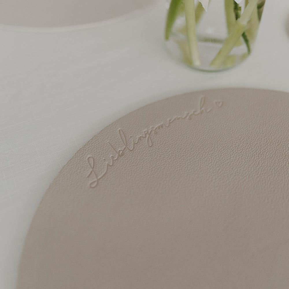 Detailaufnahme der Prägung „Lieblingsmensch“ auf einem runden cremefarbenen Platzset.