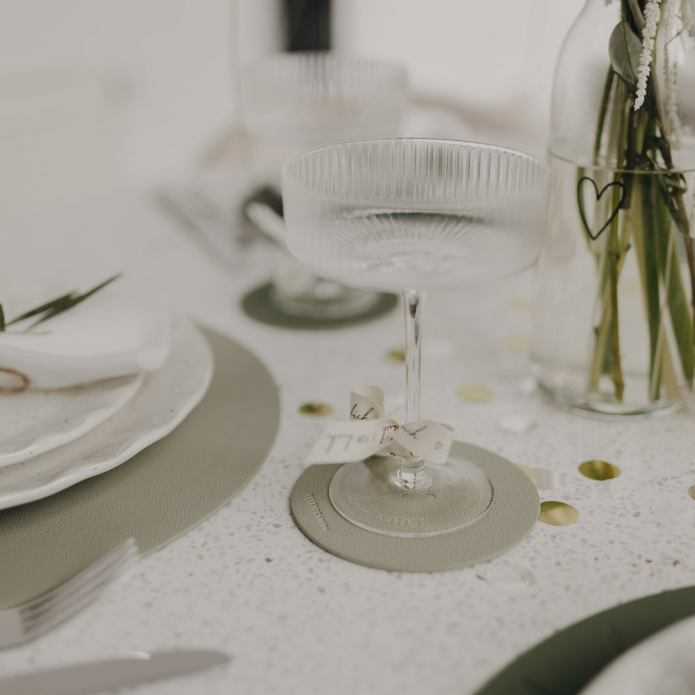 Hellgrüner Untersetzer mit Sektglas und Schleife, stilvoll aufgedeckt.