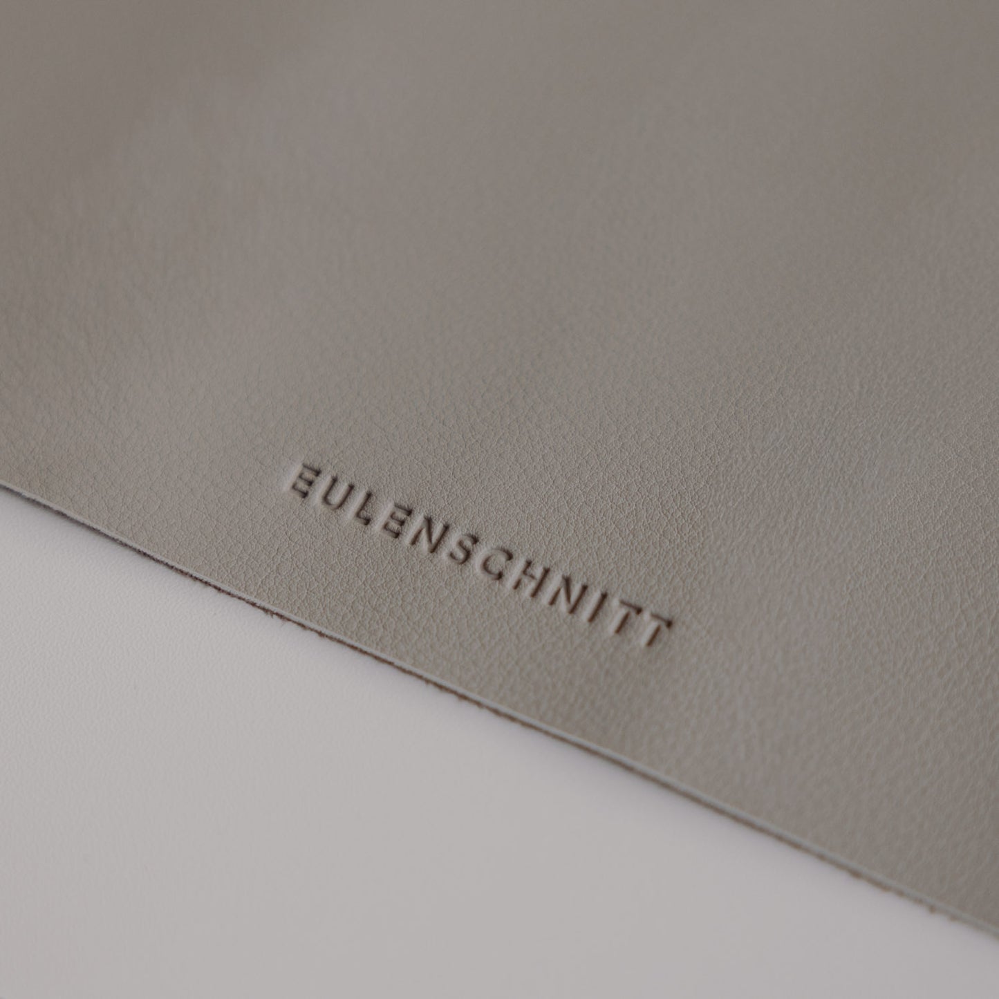 Detailaufnahme Logo Eulenschnitt auf grauer Schreibtischunterlage, hochwertige Lederoptik