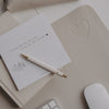 Taupe Schreibtischunterlage mit Herz-Prägung, Notizblock und Stift auf hellem Schreibtisch