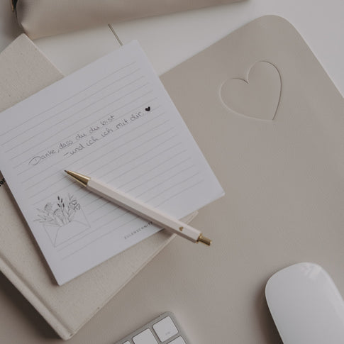 Taupe Schreibtischunterlage mit Herz-Prägung, Notizblock und Stift auf hellem Schreibtisch
