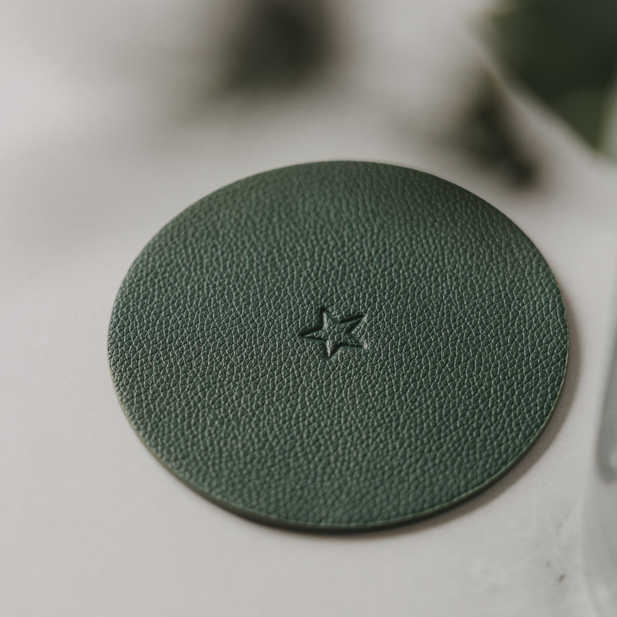 Dunkelgrüner runder Untersetzer in Lederoptik mit geprägtem Stern