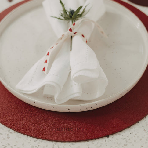 Rotes Weihnachts-Platzset unter Keramikteller mit festlich dekorierter Serviette