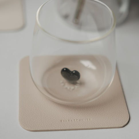 Glas mit schwarzem Herzdetail auf einem beigen quadratischen Untersetzer