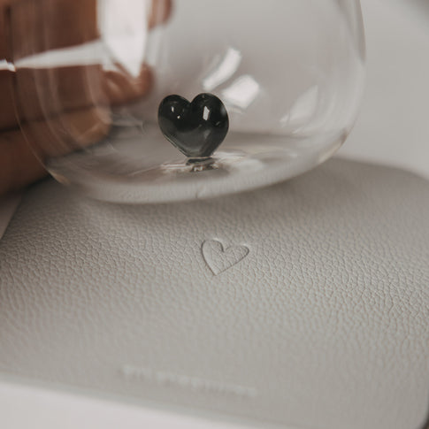 Glas mit schwarzem Herzdetail auf einem hellgrauen Untersetzer mit Herzprägung