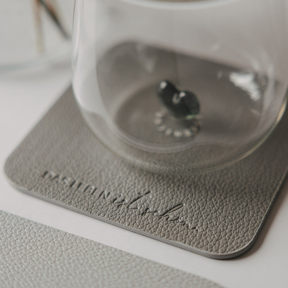 Glas auf grauem quadratischem Untersetzer in Lederoptik mit geprägtem Schriftzug