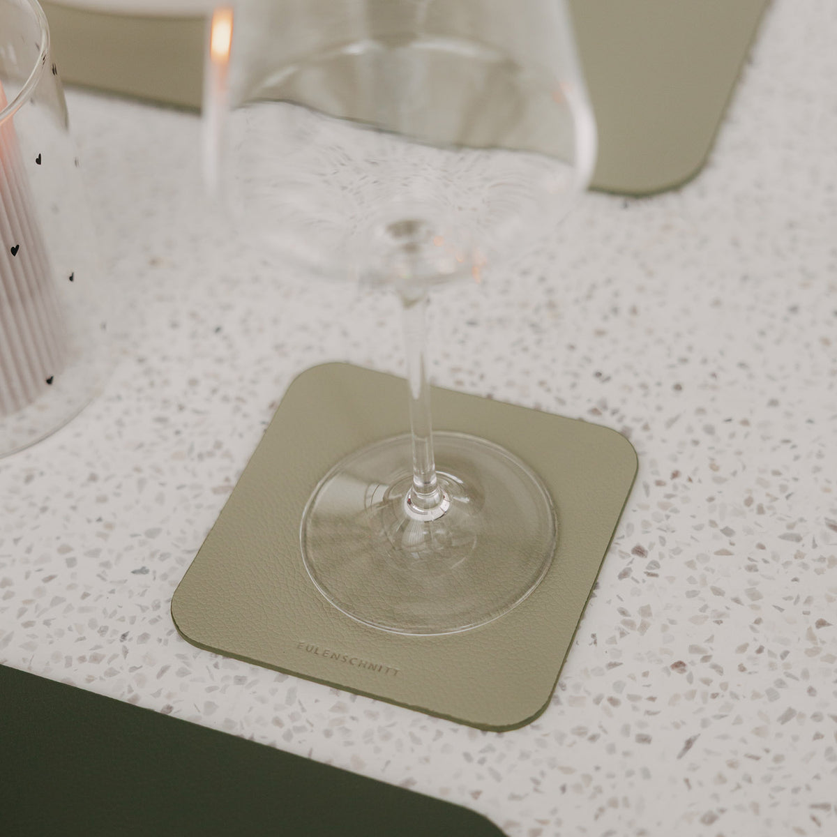 Grüner eckiger Untersetzer in Lederoptik mit Weinglas auf modern gedecktem Tisch