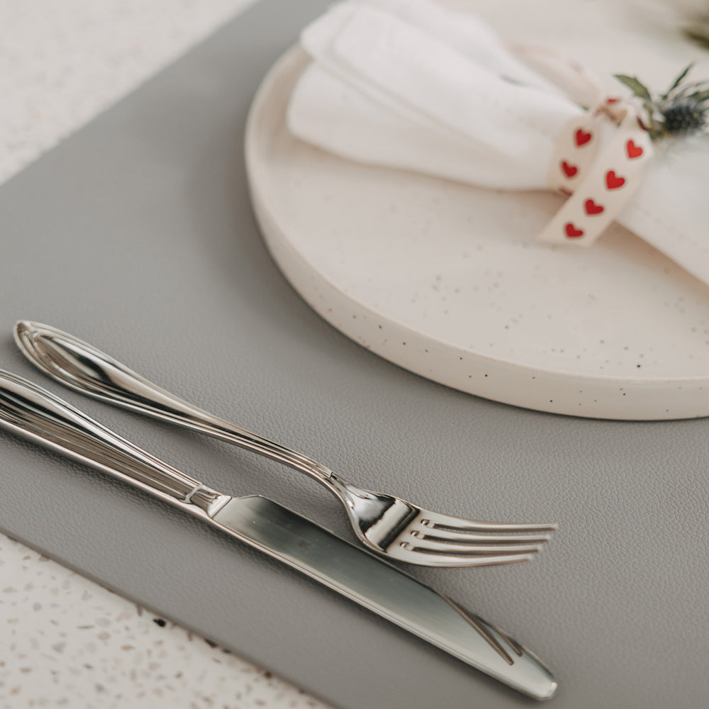 Graues Platzset in Lederoptik mit Teller, Serviette und Besteck auf gedecktem Tisch